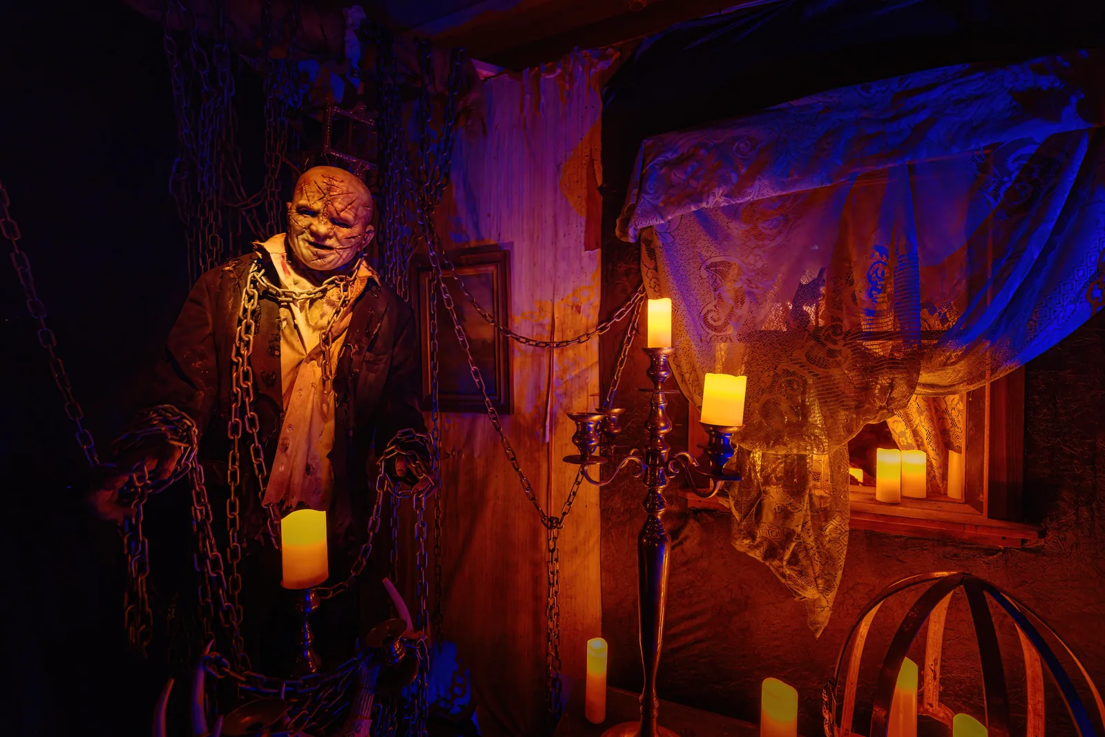Masked performer with chains among candlelit theatrical sets at a past Legends of Horror production